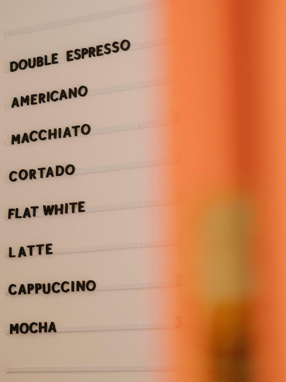 The CONA coffee menu board — letters spelling out double espresso, americano, macchiato, cortado, flat white, latte, cappuccino, mocha
