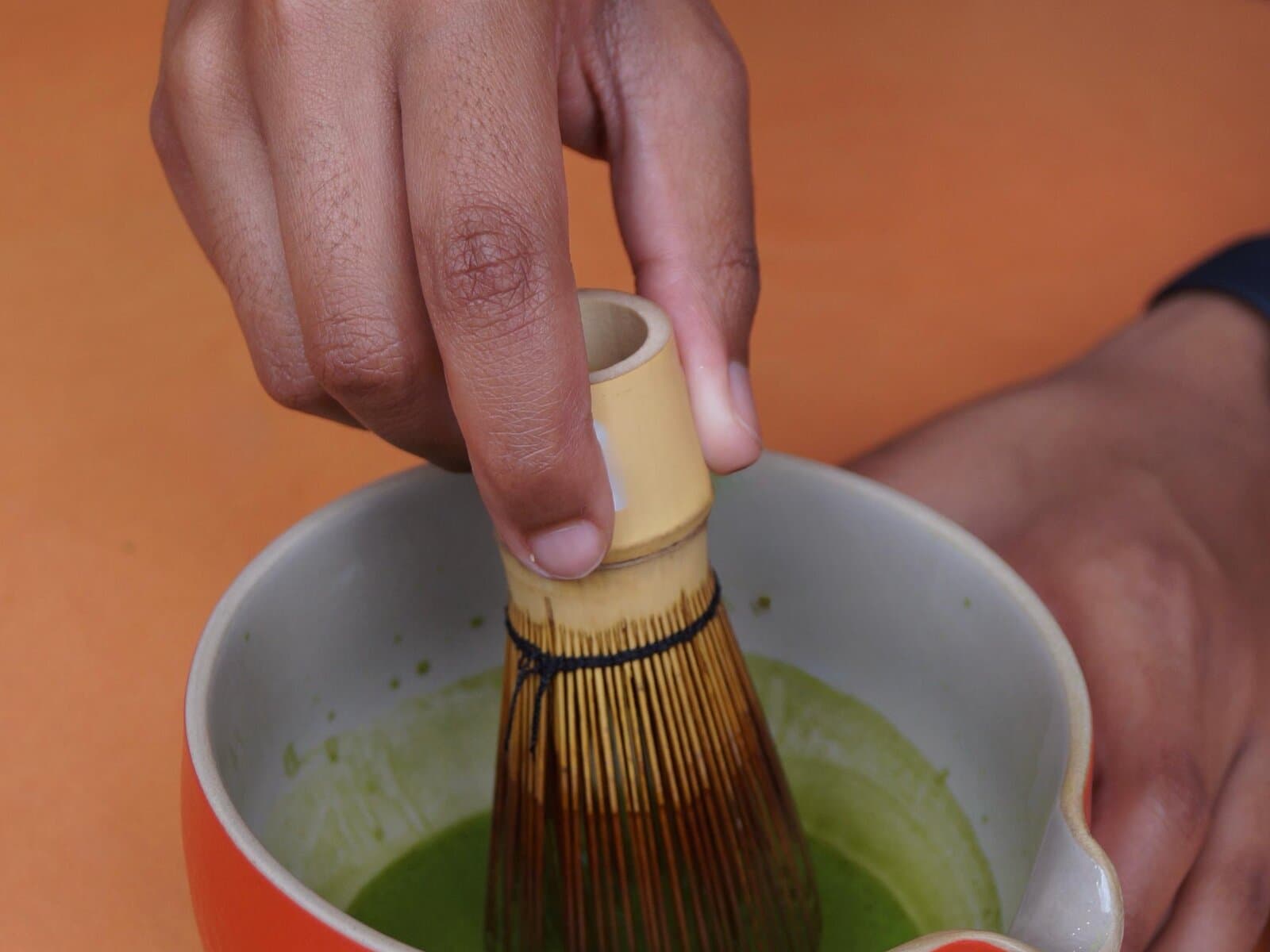 Hand-whisking matcha in a ceramic bowl with a bamboo chasen