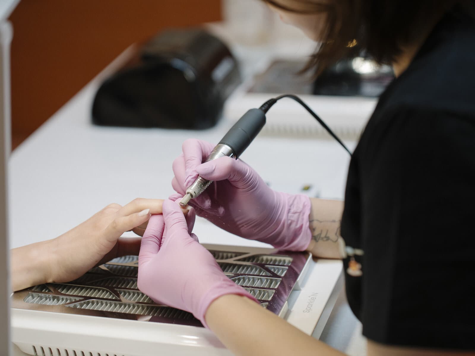 A CONA technician using an electric nail file to refine a gel finish
