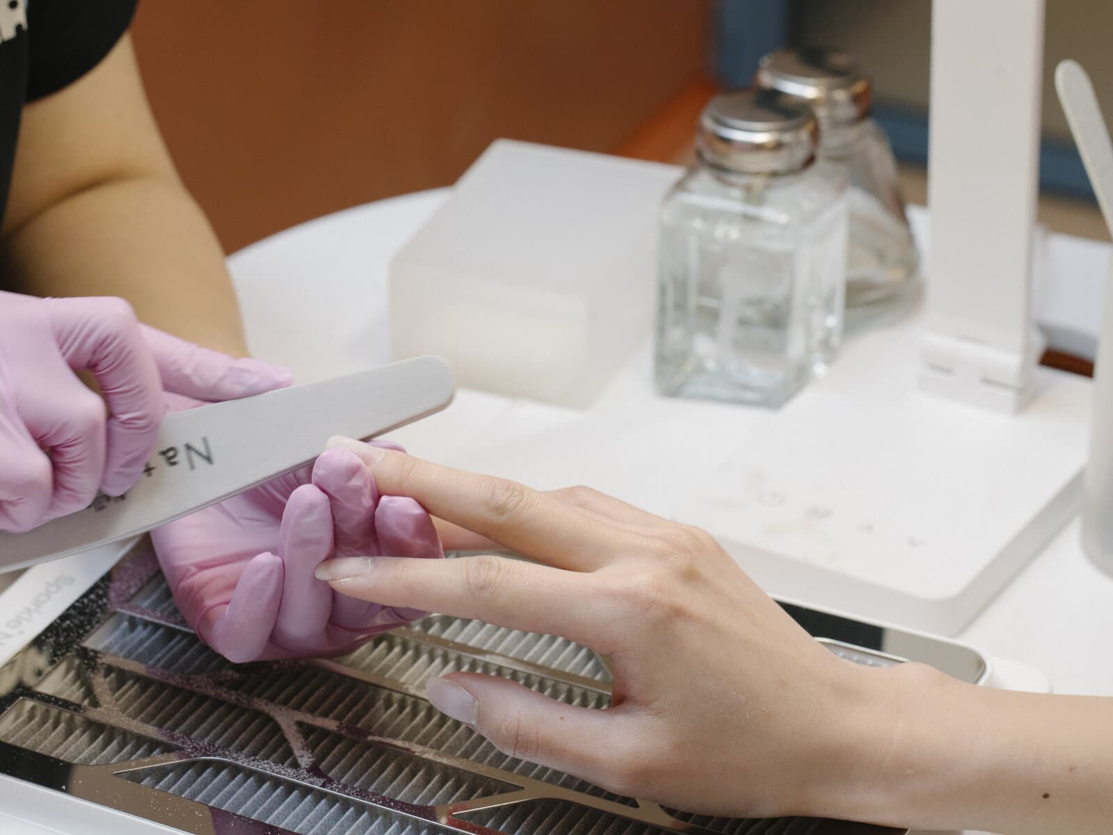 A CONA technician shaping a client's nail with a hand file